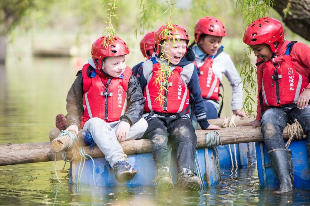 Cubs in helmets and buoyancy aids on a raft they built